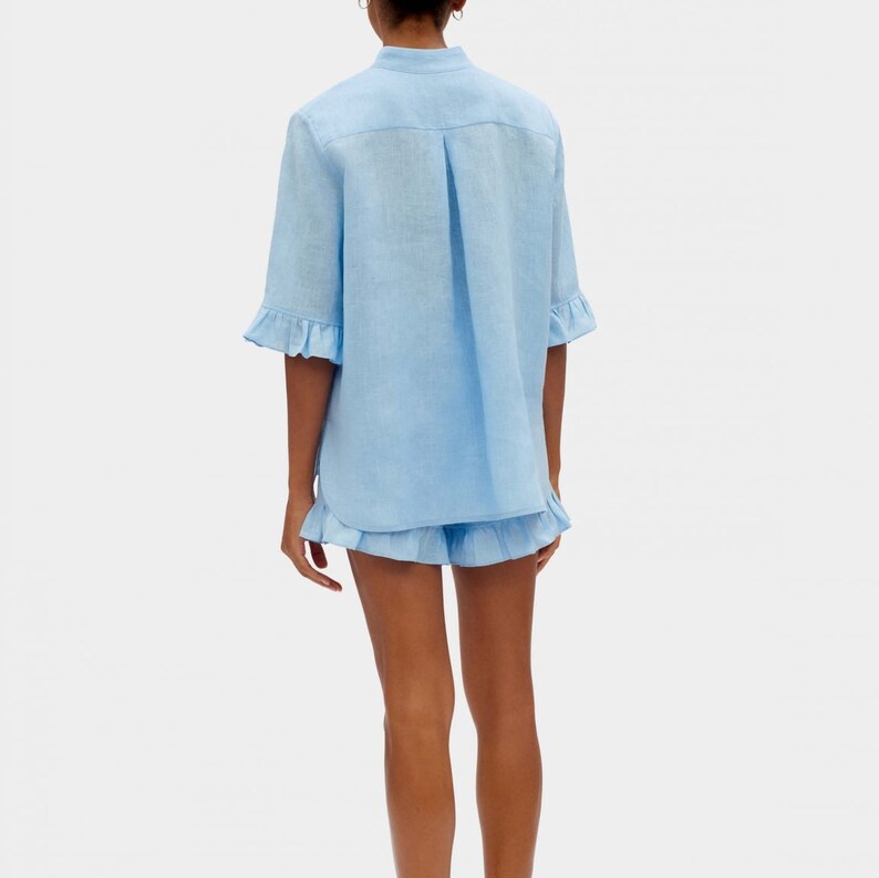 May include: A light blue linen shirt and shorts set with ruffle detailing. The shirt has a button-up front and short sleeves. The shorts have a relaxed fit and a ruffle trim.