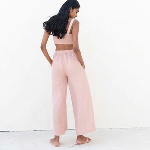 May include: A light pink linen pantsuit with a cropped top and wide-leg pants. The pants have an elastic waistband and pockets.
