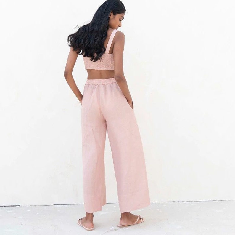 May include: A light pink linen pantsuit with a cropped top and wide-leg pants. The pants have an elastic waistband and pockets.