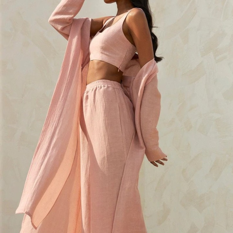 May include: A pink linen three-piece set including a long-sleeved shirt, a sleeveless top, and wide-leg pants.