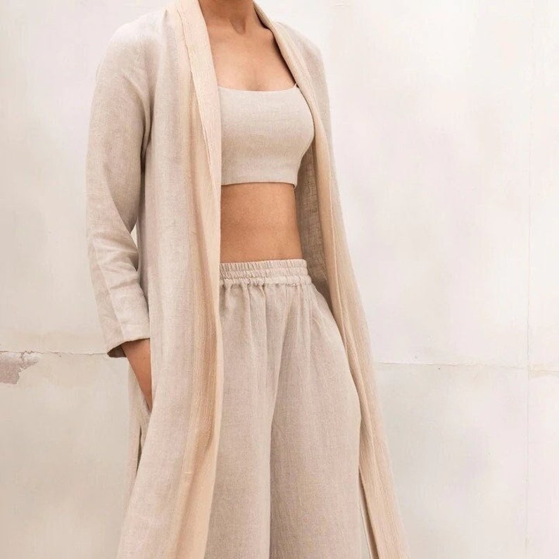 May include: A beige linen pantsuit with a long, open-front jacket and wide-leg pants. The jacket has a shawl collar and the pants have an elastic waistband.