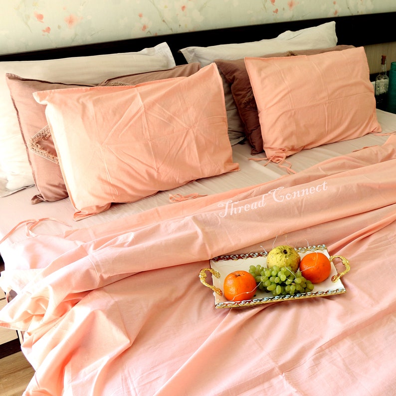 K&ouml;nnte beinhalten: Ein Bett in Pfirsichfarbe mit zwei Kissen und einer wei&szlig;en Decke. Ein Tablett mit Obst steht auf dem Bett. Der Text "Thread Connect" ist auf dem Bett sichtbar.