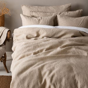 May include: A beige duvet cover set featuring a textured fabric with a visible weave. The bedding includes a large duvet cover and four matching rectangular pillowcases in a neutral tan shade, layered over a crisp white flat sheet on a bed.