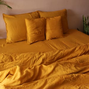 May include: A mustard yellow linen bedding set with a duvet cover and pillowcases. The bedding is arranged on a bed with pillows.