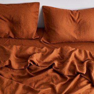 K&ouml;nnte beinhalten: Ein Bettw&auml;sche-Set aus Leinen in Rostfarbe mit einem Bettbezug und zwei Kissenbez&uuml;gen. Die Bettw&auml;sche ist zerknittert und hat einen nat&uuml;rlichen, entspannten Look.