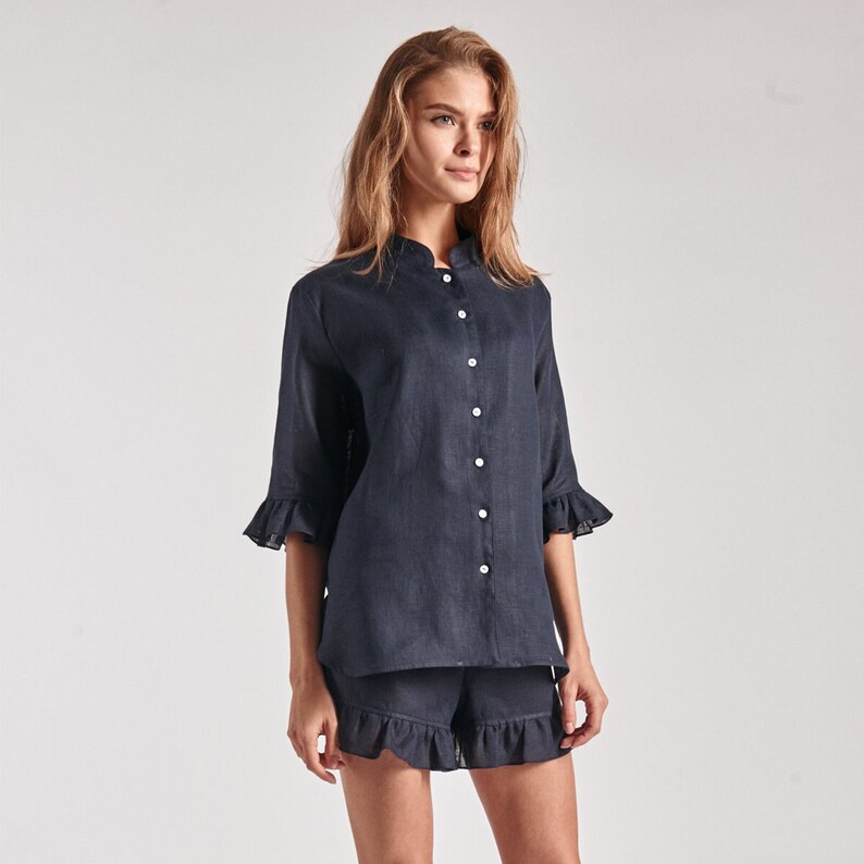 May include: A navy blue linen pajama set with a collared shirt and shorts. The shirt has a mandarin collar and button closure. The shorts have a ruffle trim.