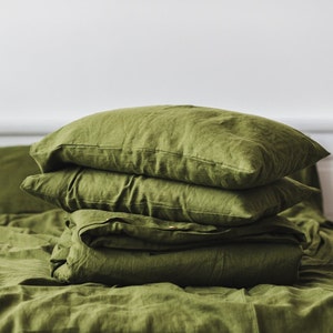 May include: A stack of three green linen pillowcases on a green linen bedspread.