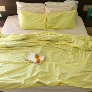 K&ouml;nnte beinhalten: Ein gelbes Bett mit einem wei&szlig;en und gelben gemusterten Bettbezug und zwei gelben Kissen. Auf dem Bett liegen drei Orangen auf einem wei&szlig;en Tablett mit goldener Verzierung.