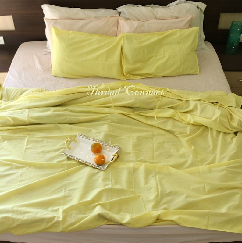 K&ouml;nnte beinhalten: Ein gelbes Bett mit einem wei&szlig;en und gelben gemusterten Bettbezug und zwei gelben Kissen. Auf dem Bett liegen drei Orangen auf einem wei&szlig;en Tablett mit goldener Verzierung.