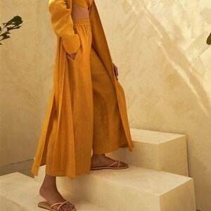 May include: A mustard yellow linen pantsuit with a long, flowing jacket and wide-leg pants. The pants have a drawstring waist and the jacket has a tie belt.