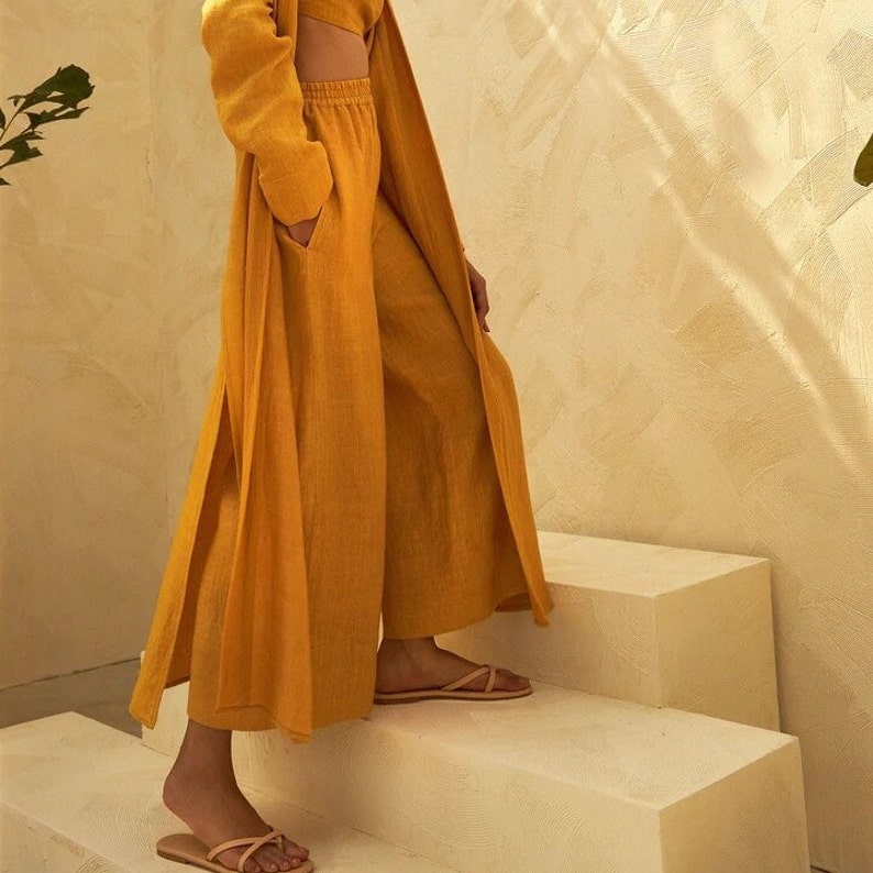 May include: A mustard yellow linen pantsuit with a long, flowing jacket and wide-leg pants. The pants have a drawstring waist and the jacket has a tie belt.