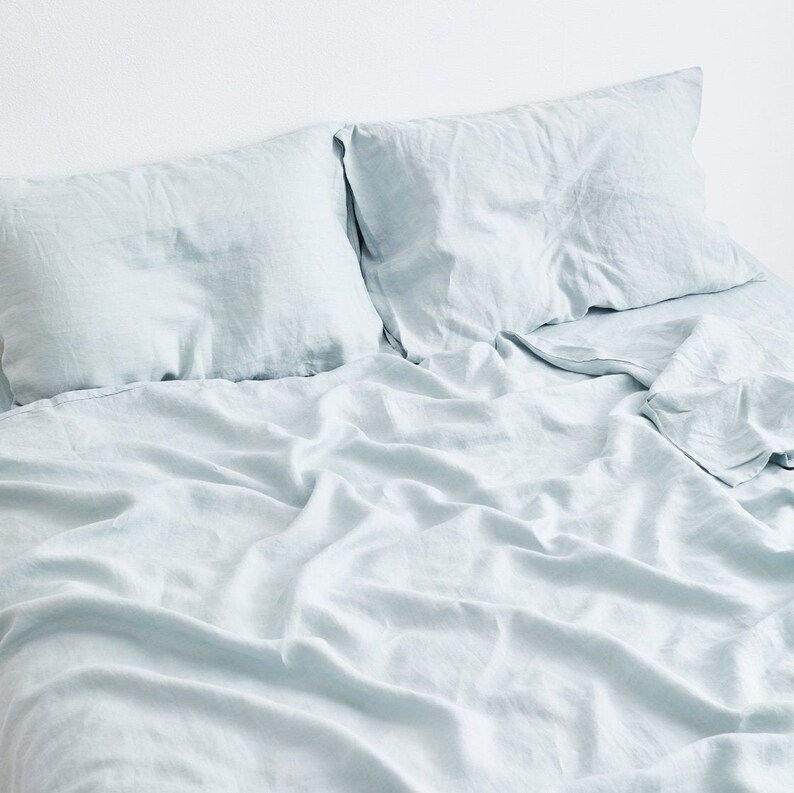 May include: A light blue linen bedding set with two pillowcases and a flat sheet. The bedding is made of soft, breathable linen and is perfect for a cool and comfortable sleep.