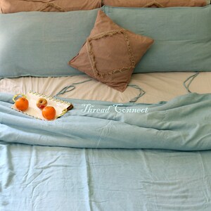 K&ouml;nnte beinhalten: Ein hellblaues Bettw&auml;sche-Set mit einem dekorativen Kissen mit Fransen. Die Bettw&auml;sche liegt auf einem Bett mit einem wei&szlig;en Laken und einem Tablett mit Obst auf der Bettw&auml;sche. Der Text "Thread Connect" ist auf der Bettw&auml;sche sichtbar.