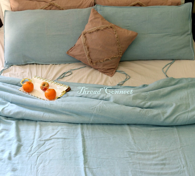 K&ouml;nnte beinhalten: Ein hellblaues Bettw&auml;sche-Set mit einem dekorativen Kissen mit Fransen. Die Bettw&auml;sche liegt auf einem Bett mit einem wei&szlig;en Laken und einem Tablett mit Obst auf der Bettw&auml;sche. Der Text "Thread Connect" ist auf der Bettw&auml;sche sichtbar.