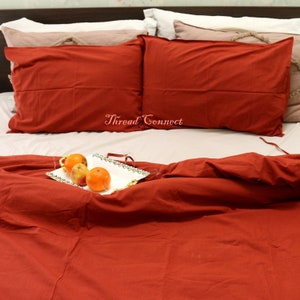 K&ouml;nnte beinhalten: Ein roter Bettbezug und zwei rote Kissenbez&uuml;ge auf einem Bett mit einem wei&szlig;en Tablett mit Orangen auf dem Bettbezug. Der Text "Thread Connect" ist auf dem Bett sichtbar.