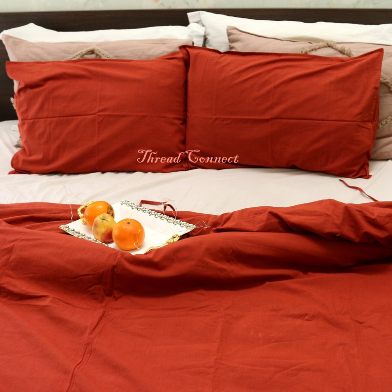 K&ouml;nnte beinhalten: Ein roter Bettbezug und zwei rote Kissenbez&uuml;ge auf einem Bett mit einem wei&szlig;en Tablett mit Orangen auf dem Bettbezug. Der Text "Thread Connect" ist auf dem Bett sichtbar.