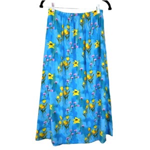 May include: A long, flowing skirt with a vibrant blue background adorned with a floral pattern. The design features yellow daffodils and small purple flowers. The skirt is hanging on a black hanger.