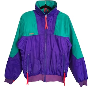 May include: A retro colour-blocked jacket in teal, purple, and magenta. The jacket features a high collar, a full-length zip, and two front pockets. The cuffs and waistband are ribbed. The jacket has a sporty aesthetic.