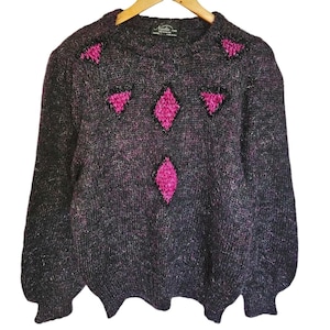 May include: A black and pink fuzzy sweater with a geometric design. The sweater has a crew neck and long sleeves.