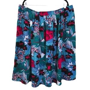May include: A knee-length skirt with a vibrant tropical floral print. The skirt features a pleated design with a mix of teal, blue, pink, and black floral and leaf patterns. It hangs from a black hanger against a white background.