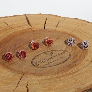 Pode incluir: Quatro pares de brincos de cerâmica com diferentes designs. Os brincos são exibidos em uma superfície de madeira. O texto "Philina naturali - handmade jewelry" é visível na superfície.
