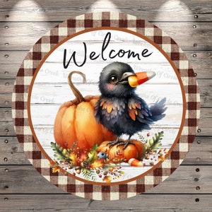May include: A round welcome sign with a brown and white checkered border. The center features a whitewashed wood background with the word "Welcome" in black script. A black crow with a candy corn beak sits on a pumpkin with fall leaves and acorns around it.