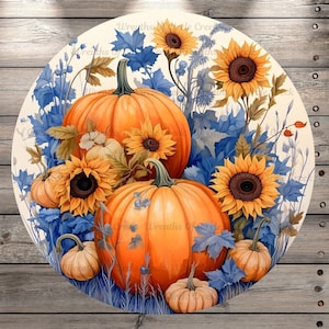 May include: A round decorative piece featuring a watercolor design of pumpkins and sunflowers. The pumpkins are orange, and the sunflowers are yellow with brown centers. Blue leaves and foliage surround the pumpkins and sunflowers. The background is a light beige color.