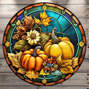 May include: A stained glass round design featuring two orange pumpkins, a sunflower, and fall leaves in shades of green, yellow, and brown. The background is a teal blue.
