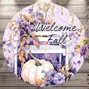 May include: A round, purple and gold welcome sign with the text "Welcome Fall" in white. The sign features a white bench with a pumpkin and fall foliage.