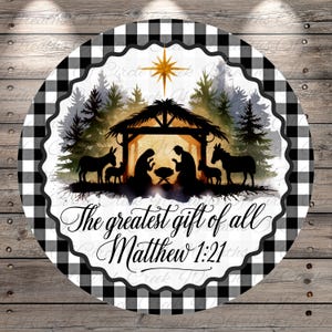 May include: A round decorative sign with a black and white buffalo check border. The center features a silhouette of the Nativity scene with the text "The greatest gift of all Matthew 1:21". A gold star is at the top.
