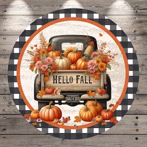 May include: Round decorative sign featuring a black truck bed filled with pumpkins, flowers, and fall foliage. The text "HELLO FALL" is displayed on the truck bed. The sign has a black and white buffalo check border with an orange accent.