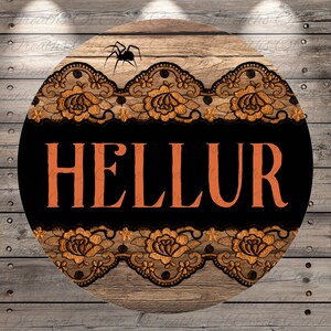 May include: Round wooden sign with the word "HELLUR" in orange letters on a black background, framed by orange and black lace. A black spider is at the top. The sign has a rustic, Halloween theme.