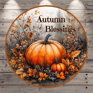 May include: A round wooden sign with a watercolor painting of two pumpkins, fall leaves, and the text "Autumn Blessings".
