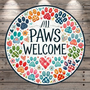 May include: A round sign with the words "ALL PAWS WELCOME" in black script, surrounded by colorful paw prints, hearts, and flowers. The paw prints are in various patterns and colors, including blue, red, orange, and green. The sign is set against a wooden background.
