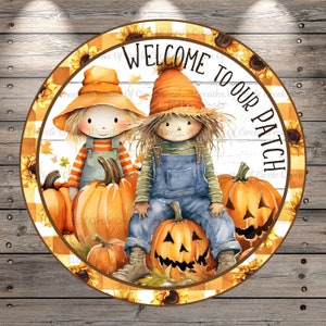 May include: A round sign with a white background and a checkered border. The sign features two scarecrows, one sitting on a pumpkin and the other standing next to a pumpkin. The sign says "Welcome to our patch" in a brown font.