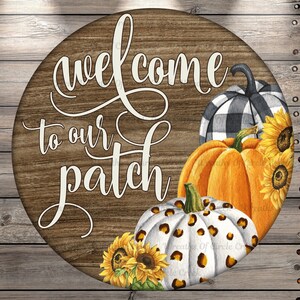 May include: Round wooden sign with the text "welcome to our patch". The sign features watercolor pumpkins in orange, white with leopard print, and black and white plaid. Sunflowers are also included in the design.