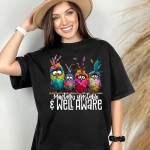 Pode incluir: Camiseta preta com um gráfico de quatro pássaros coloridos empoleirados em um galho. O texto "Mentally Unstable & Well Aware" é impresso abaixo dos pássaros.
