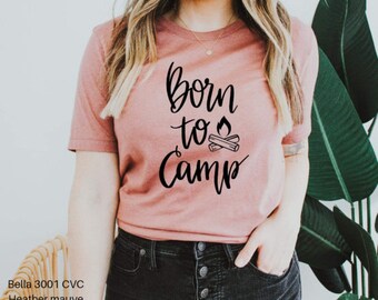 May include: A heather mauve t-shirt with the text "Born to Camp" in black script. A campfire graphic with flames is included in the text.