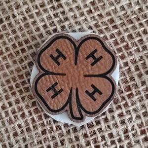 May include: A brown wooden four-leaf clover with the letter "H" in each leaf.
