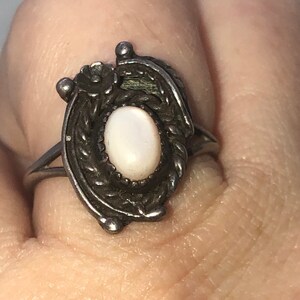 May include: A silver ring with a white pearl-like stone set in a floral design.