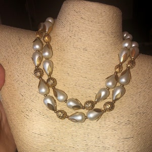 Puede incluir: Un collar de perlas de doble cadena con detalles dorados. Las perlas son de forma de pera y los detalles dorados son pequeños e intrincados.