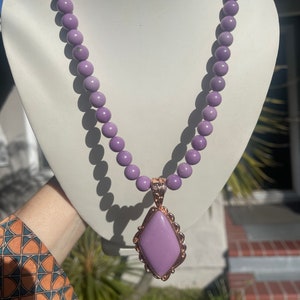 May include: A purple beaded necklace with a large, light purple gemstone pendant in a rose gold setting.