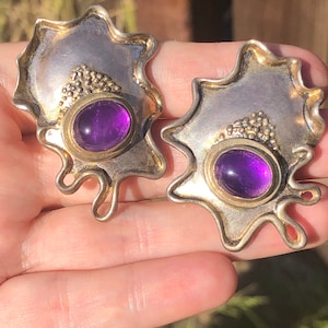 Könnte beinhalten: Ein Paar Ohrringe aus Silber und Gold mit jeweils einem violetten Amethyststein. Die Ohrringe sind tropfenförmig.