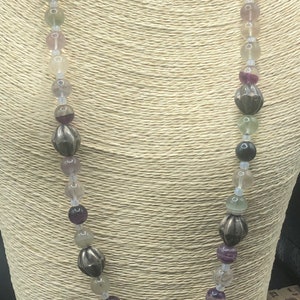 May include: A multi-colored gemstone necklace with a silver butterfly pendant. The necklace features round beads in shades of green, purple, and white. The butterfly pendant has intricate details and a textured finish.