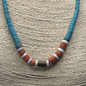 May include: A turquoise, white, and coral beaded necklace with a silver accent. The necklace is on a woven background.