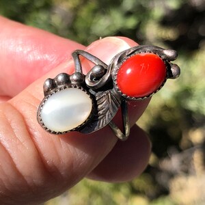 May include: A silver ring with a red coral and a white mother of pearl stone. The ring has a delicate floral design.