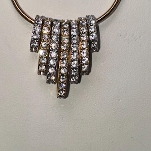 May include: A gold chain necklace with a pendant made of multiple rows of small, clear stones.