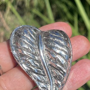 May include: A silver leaf-shaped brooch with a detailed textured design.