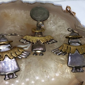 May include: A set of silver and gold angel earrings and a pendant. The angel figures have wings and halos. The earrings have a hook fastening.