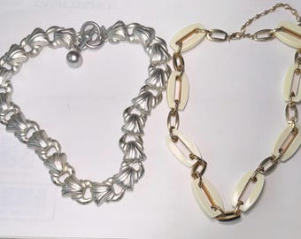 Puede incluir: Dos collares, uno plateado con diseño de concha y otro dorado con eslabones ovalados blancos.